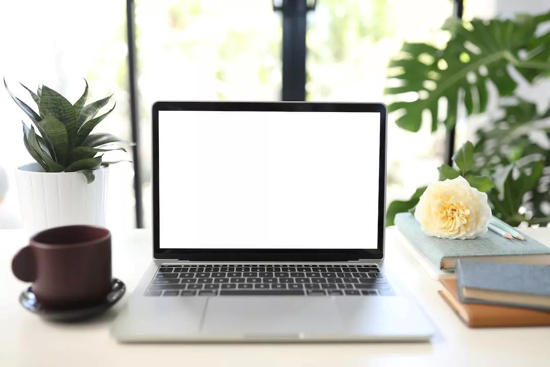 A laptop on a desk with books and a cup of coffee